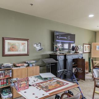 A cozy living room featuring shelves with board games, a large television, and various artwork on the walls.