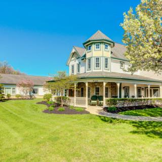 A beautiful Victorian-style house with a wraparound porch and manicured lawn on a sunny day.