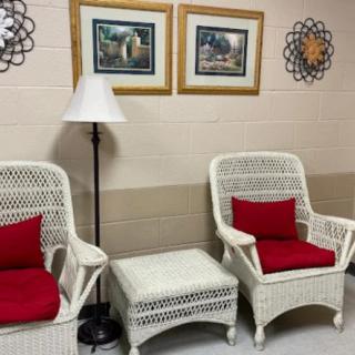 A cozy seating area with wicker chairs and red cushions accompanied by a floor lamp, framed art, and wall decor.