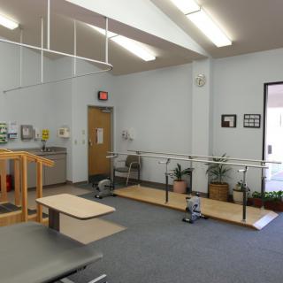 A physical therapy clinic with exercise equipment and parallel bars for rehabilitation exercises.