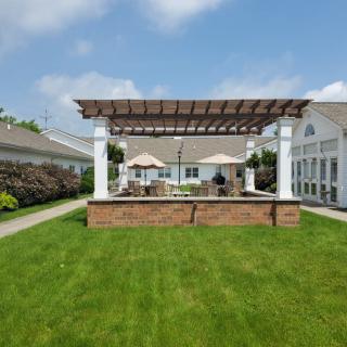A sunny yard featuring a pergola with patio seating and well-manicured lawn.