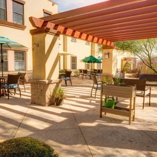 A sunny outdoor patio with a pergola, featuring tables and chairs near a building exterior.