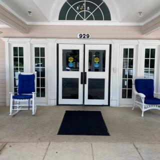 A building entrance with double doors, flanked by two blue rocking chairs.