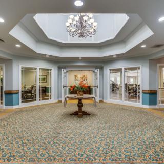 A spacious lobby area with a chandelier, central table, and carpeted floor.