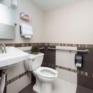 A clean and modern bathroom with a toilet, sink, mirror, towel dispenser, and grab bars.