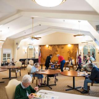 A community dining room with seniors seated at tables, enjoying a meal together.