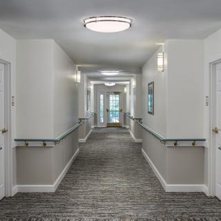 A brightly lit hallway with doors lining both sides and a carpeted floor.