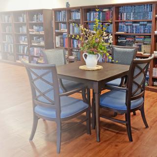 A cozy reading area in a library with bookshelves filled with books and a table surrounded by chairs.