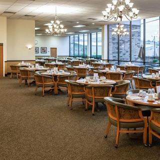 An elegant dining room with neatly arranged tables and chairs, illuminated by chandeliers.