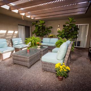 A cozy patio with comfortable outdoor furniture and lush green plants illuminated by natural sunlight under a pergola.