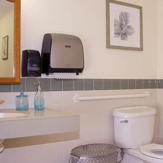 A clean bathroom with a toilet, sink, mirror, and paper towel dispenser.
