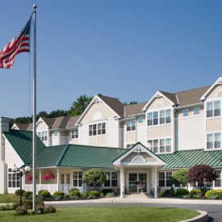 A residential-style building with a green roof and an American flag in front, surrounded by well-maintained landscaping.