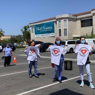 A group of people wearing masks, holding t-shirts, gathered in a parking lot.
