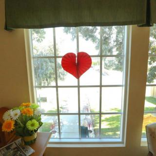 A heart-shaped decoration on a sunlit window with flowers nearby.