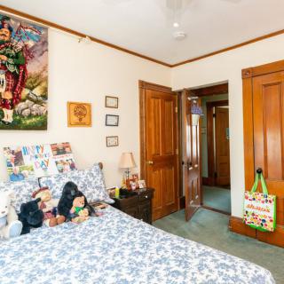 A cozy bedroom featuring a bed with patterned bedding, decorated with stuffed animals, surrounded by wooden doors and walls adorned with artwork and photographs.