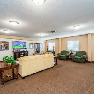 A spacious and well-lit living room featuring a beige sofa, two green armchairs, a television, and tasteful decor.