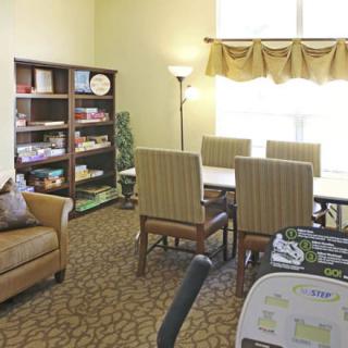 A cozy living room with a sofa, bookshelves, a table surrounded by chairs, and a standing lamp.