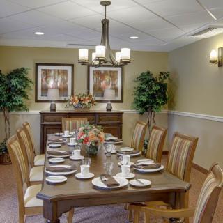 A formal dining room with a long table set for a meal, surrounded by chairs and decorated with plants and artwork.