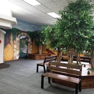 A cozy indoor seating area with benches and artificial trees, complemented by a scenic mural on the wall.