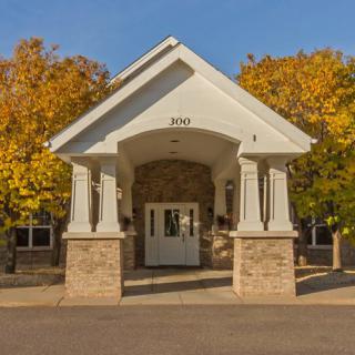 A building entrance with white pillars, surrounded by autumn foliage.