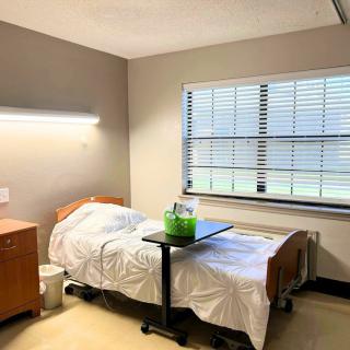 A clean and organized hospital room with a bed, nightstand, and window.