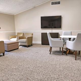A contemporary living room featuring a seating area with armchairs, a round table with chairs, and a wall-mounted television.