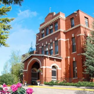 A historic brick building surrounded by trees and flowers under a clear blue sky.