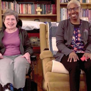 Two people smiling in a cozy living room with bookshelves in the background.