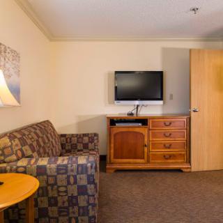 A cozy hotel room featuring a couch, television, and wooden dresser.