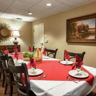 A warmly decorated dining room with a table set for six, featuring a red and white tablecloth and neatly folded napkins.
