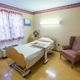 A cozy patient room in a hospital, featuring a bed, chair, and natural light.