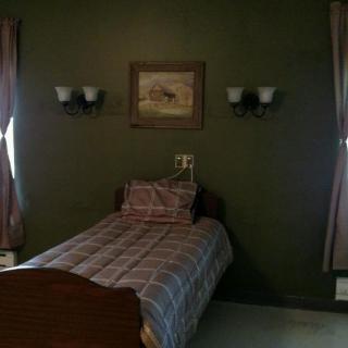 A cozy bedroom featuring a single bed with plaid bedding, surrounded by dark green walls and illuminated by wall-mounted lamps.