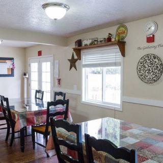A cozy dining room with multiple tables and chairs, adorned with decorative items and ample natural light from the windows.