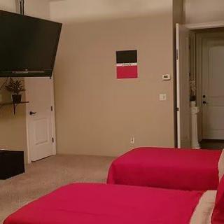 A bedroom featuring twin beds with red bedding, a mounted television, and minimalist wall decor.