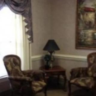A cozy corner of a living room with two patterned chairs, a small table with a lamp, and a large painting on the wall.