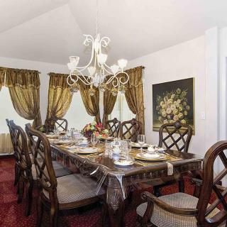 An elegant dining room featuring a large wooden table, ornate chandelier, and luxurious drapery.