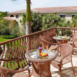 A sunny outdoor balcony with wicker tables and chairs overlooking a lush garden.