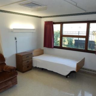 A minimalist room with a single bed, chair, and window.