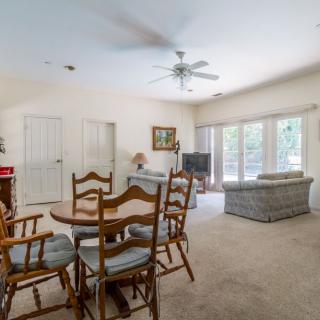 A spacious living and dining area with a ceiling fan, carpet flooring, and large windows.