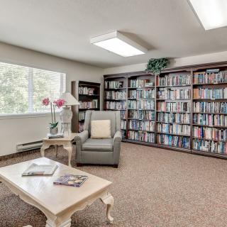 A cozy reading room with bookshelves, an armchair, and a table under soft lighting.