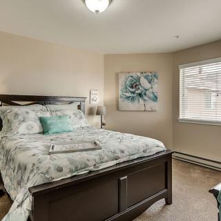 A cozy bedroom featuring a comfortable bed with patterned bedding, artwork on the wall, and natural light coming through the window.