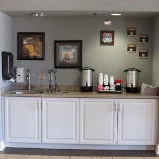 A neatly organized coffee station with white cabinets, featuring coffee pots, cups, and wall art.