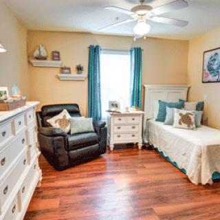 A cozy bedroom with a bed, armchair, and wooden furniture, featuring teal curtains and decorative elements.