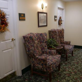 A cozy hallway with two floral armchairs, a small round table with a plant, and decorative wall accents.