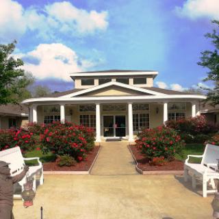 A charming residential building surrounded by colorful flowers and greenery under a bright sky.