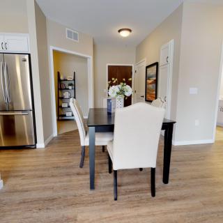 A modern dining area with a black table, beige chairs, and wood flooring next to a kitchen.