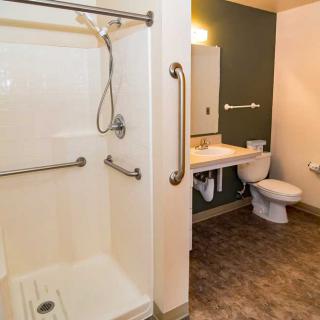 An accessible bathroom featuring a walk-in shower with grab bars, a toilet, and a sink with a mirror.