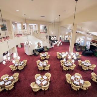 An elegant restaurant interior with tables set on a red carpeted floor and chandeliers hanging from the ceiling.