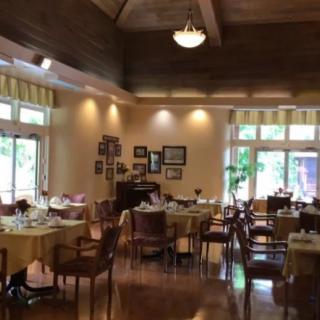 A cozy restaurant interior with neatly arranged tables and chairs, featuring warm lighting and large windows.