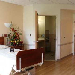 A hospital room with a bed, flowers on the table, and an open door to a bathroom.